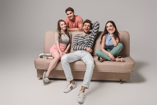 smiling young friends sitting on sofa on grey  - Photo, Image