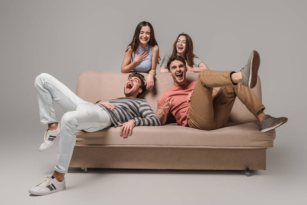 happy friends laughing and relaxing on sofa on grey  - Photo, Image