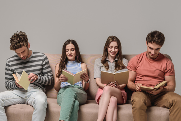 Nuoret ystävät lukemassa kirjoja istuessaan sohvalla harmaalla
 - Valokuva, kuva