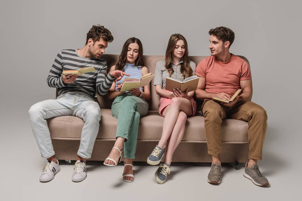 friends talking and reading books while sitting on sofa on grey - Φωτογραφία, εικόνα