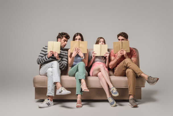 friends holding books while sitting on sofa on grey - Foto, imagen