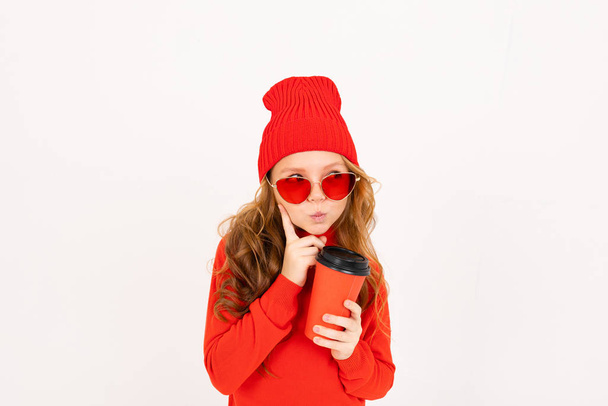 schattig meisje in rode bril poseren met koptelefoon en houden Paper cup in de studio op lichte achtergrond  - Foto, afbeelding