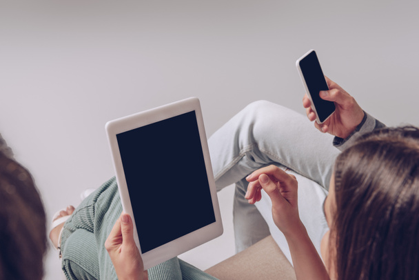 обрезанный вид пары с помощью смартфона и цифрового планшета с пустыми экранами, сидя вместе изолированы на сером
 - Фото, изображение