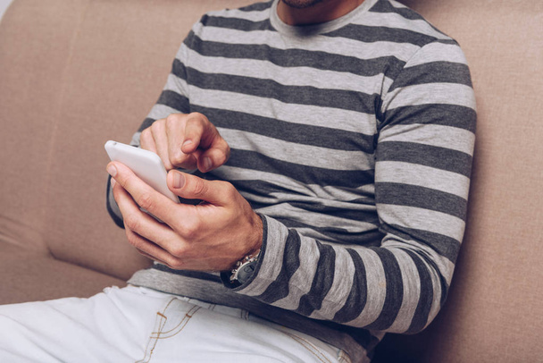partial view of man using smartphone and sitting on sofa - Foto, Imagem