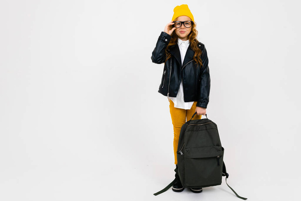 δροσερό μικρό κορίτσι σε σακάκι λέιζερ ποζάρουν με σακίδιο στο στούντιο στο φως φόντο  - Φωτογραφία, εικόνα