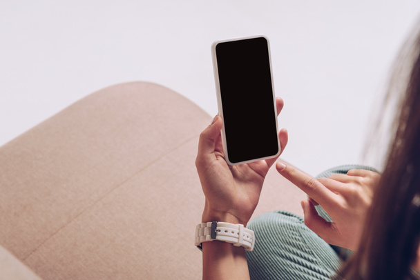 cropped view of girl using smartphone with blank screen while sitting on sofa isolated on grey - Photo, Image