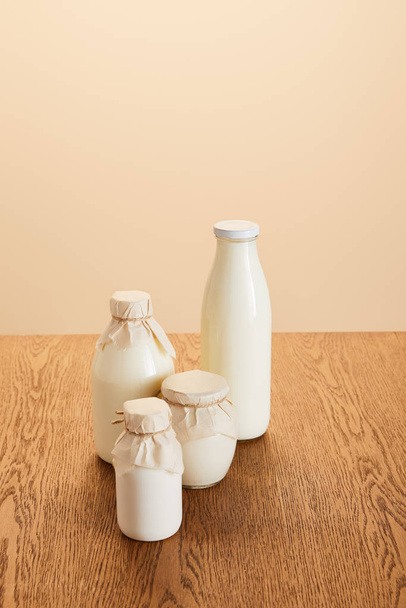 ízletes bio tejtermékek palackozva rusztikus fából készült asztalon, bézsen elkülönítve - Fotó, kép