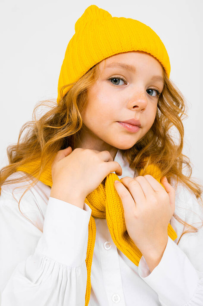 portrait of fashionable cute little girl posing against light background wearing yellow hat and scarf  - Photo, Image