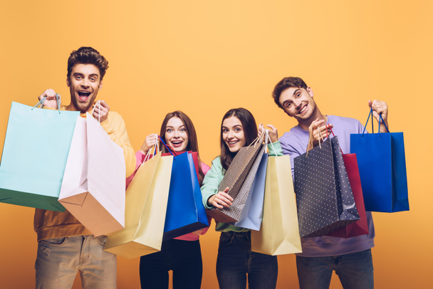 amigos felices sosteniendo bolsas de compras juntas, aisladas en amarillo
 - Foto, imagen
