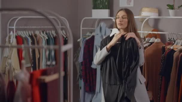 Nuori Brunette vaatekaupassa Valitsee mekko roikkua Hanger ja kokeilee sitä. Osta mekko myymälästä. Etsi ja valitse vaatteita putiikissa
. - Materiaali, video