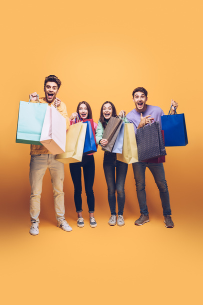 excited friends screaming and holding shopping bags together, on yellow - Foto, Bild