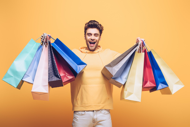 handsome excited man holding shopping bag, isolated on yellow - Фото, зображення