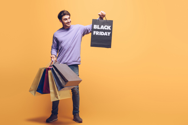happy man holding shopping bags on black friday, on yellow - Foto, imagen
