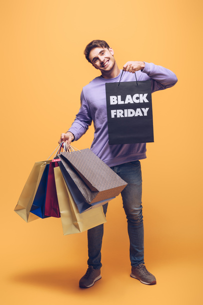 smiling man holding shopping bags on black friday, on yellow - Foto, afbeelding