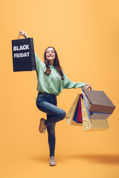 beautiful woman jumping with shopping bags on black friday, on yellow - Photo, Image
