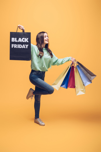 attractive girl jumping with shopping bags on black friday, on yellow - Fotoğraf, Görsel