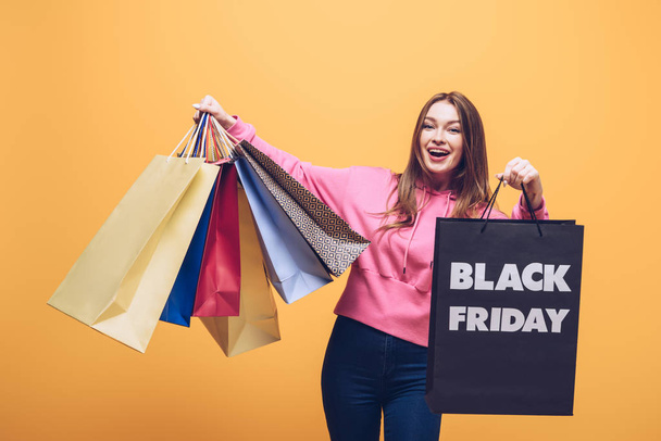 excited girl holding shopping bags on black friday, isolated on yellow - Photo, Image