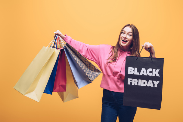 excited woman holding shopping bags on black friday, isolated on yellow - Photo, Image