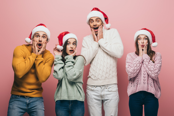 surprised friends in sweaters and santa hats, isolated on pink - Photo, Image