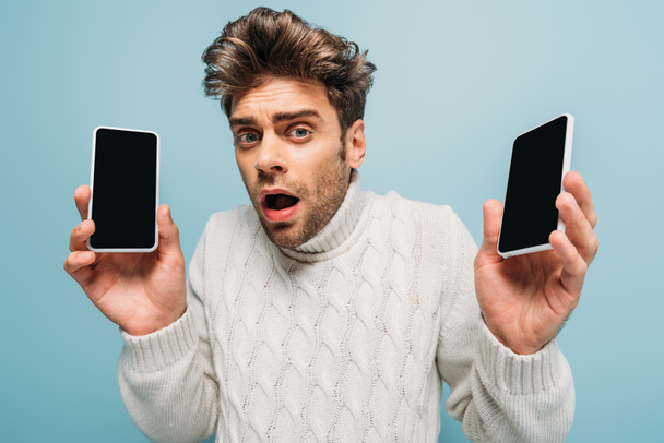 stressaantunut mies osoittaa kaksi älypuhelimet tyhjä näytöt, eristetty sininen
 - Valokuva, kuva