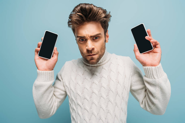 расстроенный человек показывает два смартфона с пустыми экранами, изолированные на синий
 - Фото, изображение
