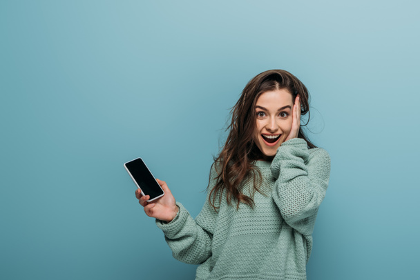 excited woman holding smartphone with blank screen, isolated on blue - Foto, afbeelding