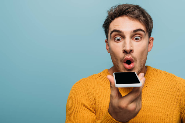 shocked handsome man using smartphone, isolated on blue - Foto, afbeelding
