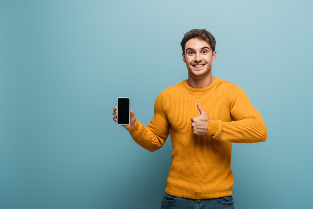 happy man showing thumb up and smartphone with blank screen, isolated on blue - Fotoğraf, Görsel