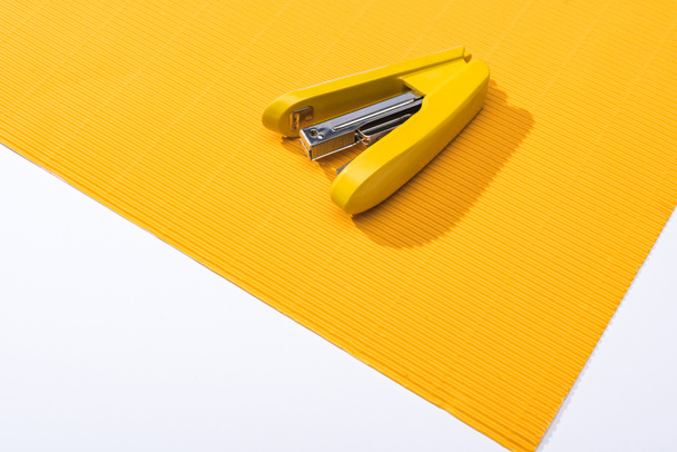 άποψη υψηλής γωνίας του κίτρινου συρραπτικού σε φωτεινό χαρτί που απομονώνεται σε λευκό  - Φωτογραφία, εικόνα