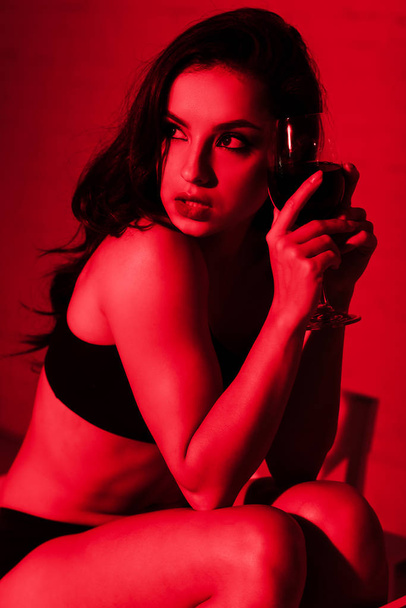 attractive seductive girl with glass of wine sitting in kitchen in red light  - Foto, Imagem
