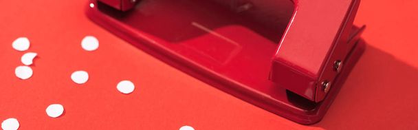 panoramic shot of holepunch with paper circles on red background  - Fotoğraf, Görsel