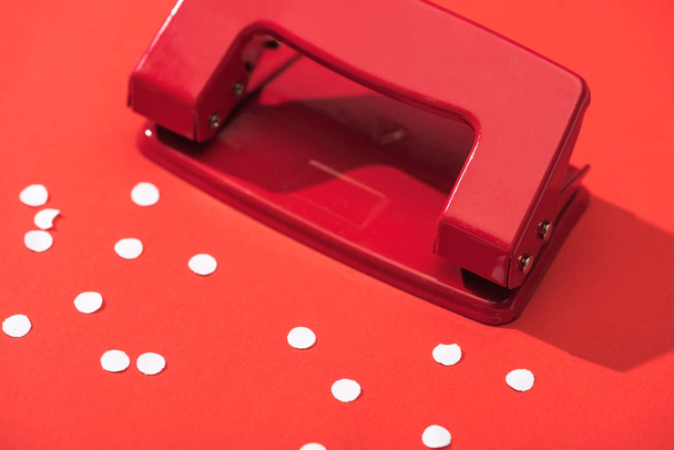 high angle view of holepunch with paper circles on red background  - Photo, Image