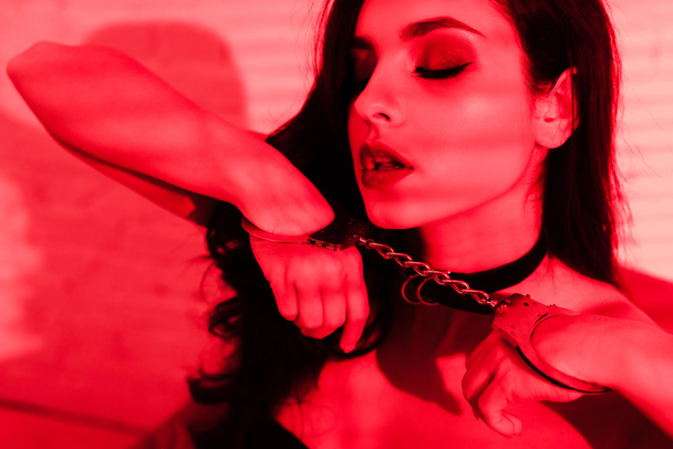 attractive seductive girl holding handcuff on red - Фото, зображення