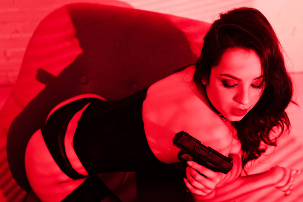 namiętna kryminalistka w body suit trzymająca pistolet na czerwono - Zdjęcie, obraz