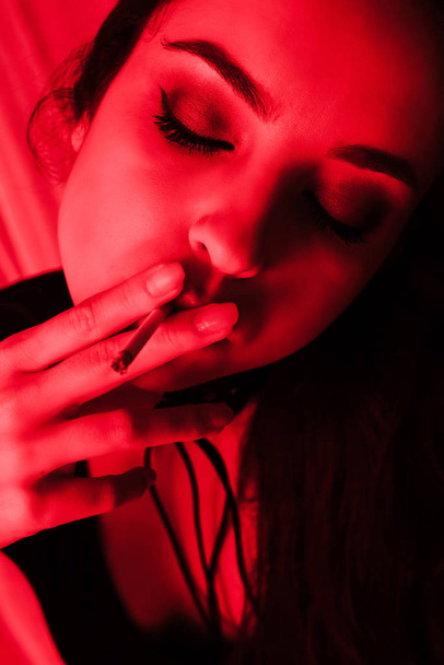 beautiful sexy girl smoking cigarette in red light - Photo, image