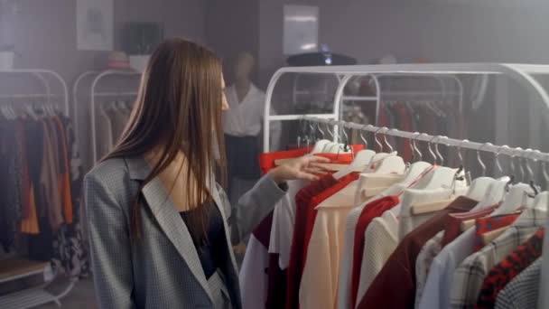 Μια νεαρή Μπρουνέτ σε ένα κατάστημα ρούχων Επιλέγει ένα φόρεμα για να κρεμάσει σε μια κρεμάστρα και το δοκιμάζει. Αγόρασε ένα φόρεμα από το μαγαζί. Αναζήτηση και επιλέξτε ρούχα σε μια μπουτίκ. - Πλάνα, βίντεο