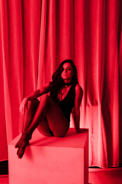 sensuele vrouw poseren in bodysuit en visnet panty 's in rood licht - Foto, afbeelding