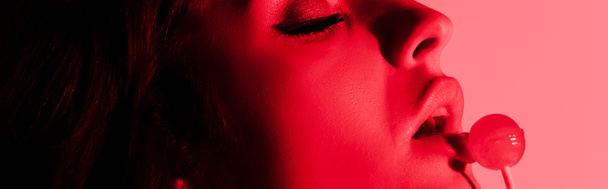 Panoramaaufnahme eines attraktiven sexy Mädchens, das Lutscher im Rotlicht isst - Foto, Bild