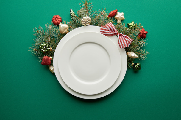 top view of white plates near festive Christmas tree branch with baubles on green background - Photo, Image
