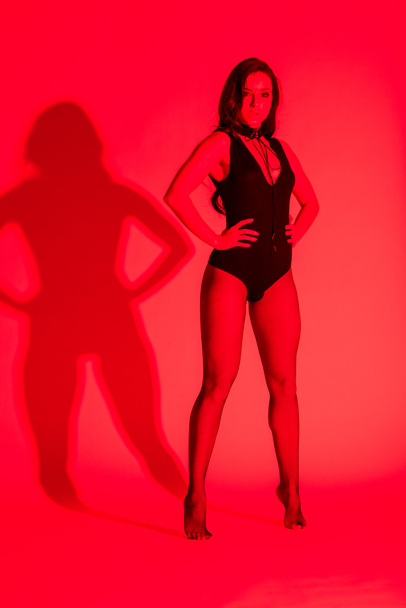 beautiful sensual young woman posing in black leotard, isolated on red - Photo, Image