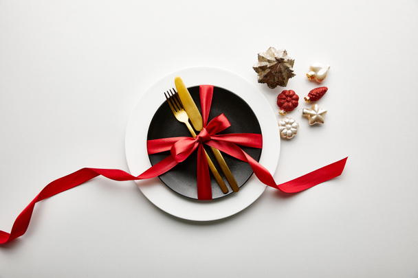 top view of white and black plates with cutlery and ribbon near festive Christmas baubles on white background - Φωτογραφία, εικόνα