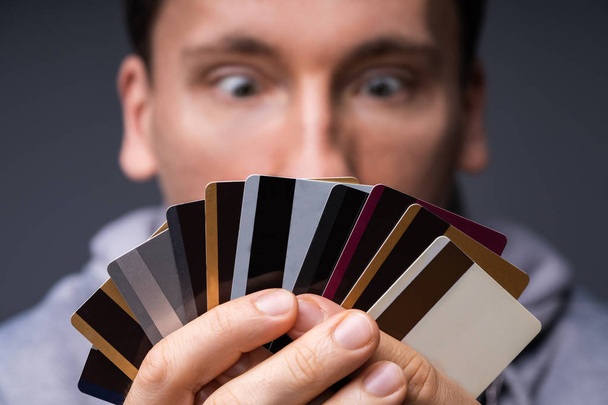 Shocked Man Looking At Too Many Credit Cards Holding In His Hand - 写真・画像