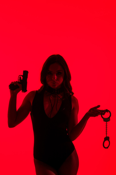 Tutkulu suçlu kadının silueti, elinde silah ve kelepçe, kırmızıda izole edilmiş. - Fotoğraf, Görsel