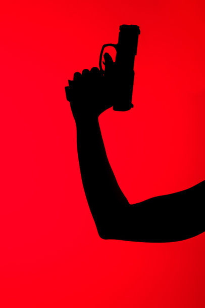 cropped view of silhouette of woman holding gun isolated on red - Foto, Imagen