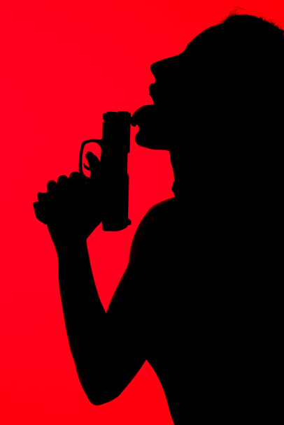 silhouette of criminal seductive woman licking gun isolated on red - Foto, afbeelding