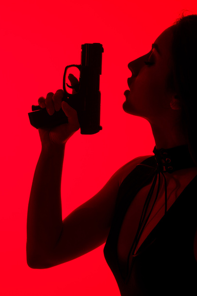 silhouette of seductive criminal woman holding gun isolated on red - Photo, Image