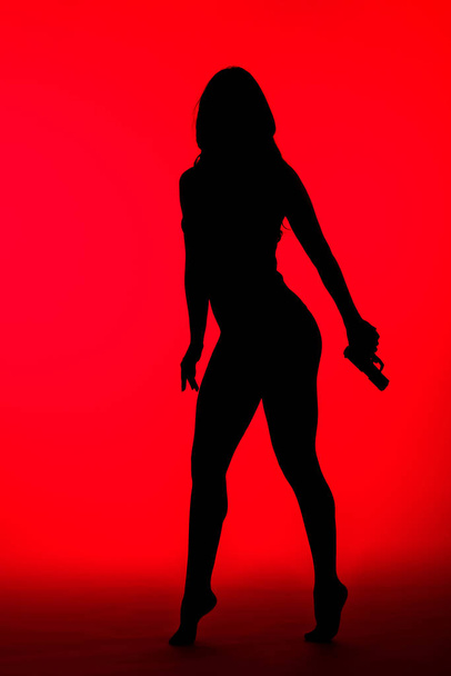 silhouette of criminal woman in bodysuit holding gun isolated on red - Foto, immagini