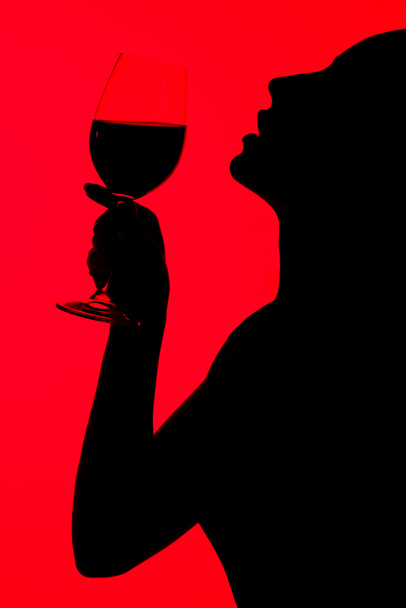 силует привабливої сексуальної жінки, що тримає келих вина ізольовано на червоному
 - Фото, зображення