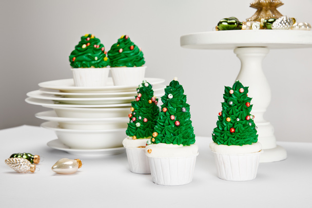Смачні різдвяні кекси з тарілками і блискучі бульбашки на білій поверхні, ізольовані на сірій - Фото, зображення