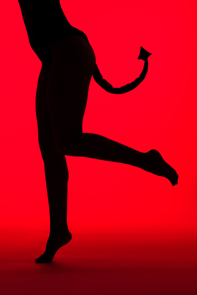 bijgesneden weergave van silhouet van sexy meisje in Duivel kostuum, geïsoleerd op rood - Foto, afbeelding